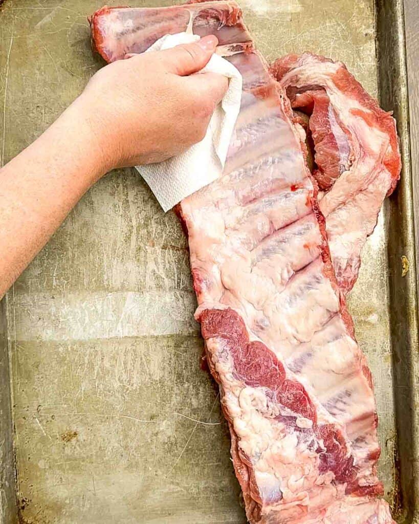 Removing the silver skin membrane from the back of a rack of pork ribs with a butter knife and paper towel.