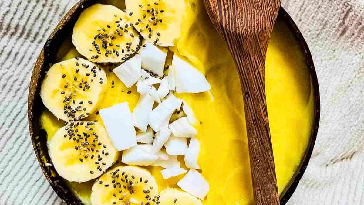 A peach smoothie bowl topped with sliced bananas, coconut, and chia seeds.