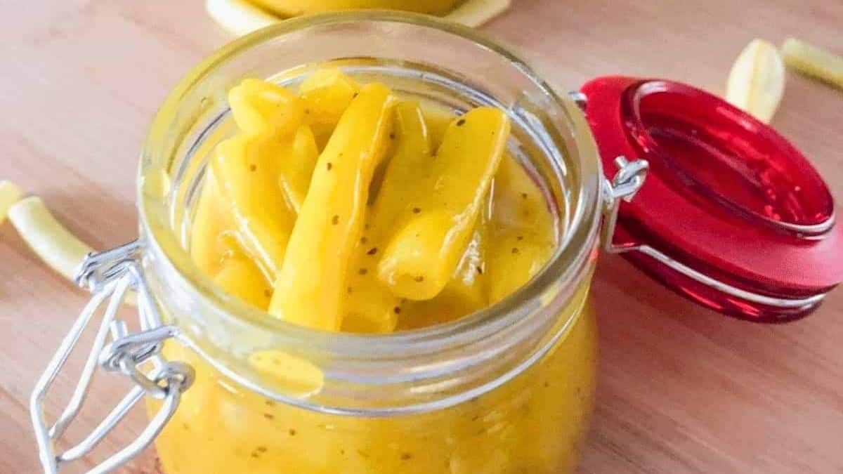 Mustard bean pickles in a canning jar with a red lid, placed on a bamboo cutting board.