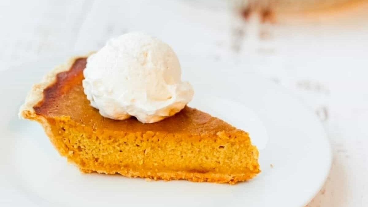 A slice of smoked pumpkin pie on a white dinner plate with a scoop of whipped cream on top.