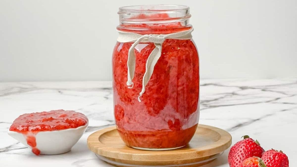 A jar of low sugar strawberry jam in a canning jar, with fresh strawberries beside it.