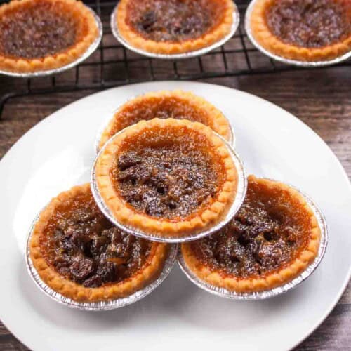Classic Canadian butter tarts stacked on a white plate, with more tarts on a wire cooling rack.