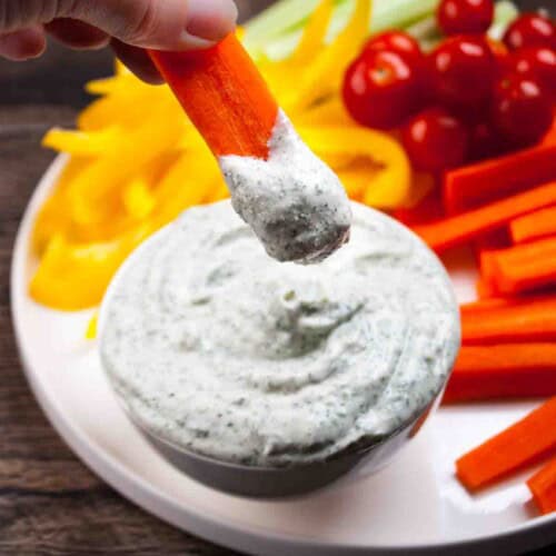 The cottage cheese ranch dip being scooped with a carrot stick, showing creamy texture.