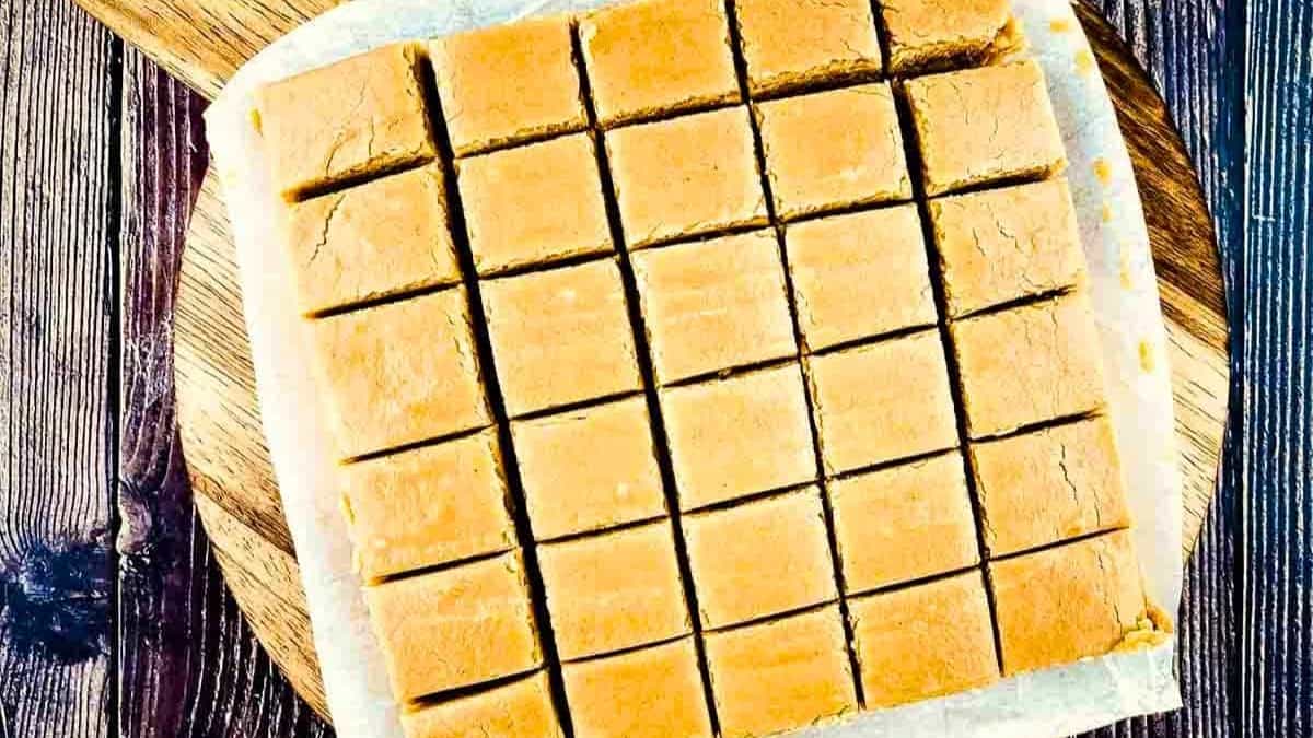 Squares of creamy peanut butter fudge arranged in neat rows, their smooth tops showing gentle swirls and a rich golden-brown color.