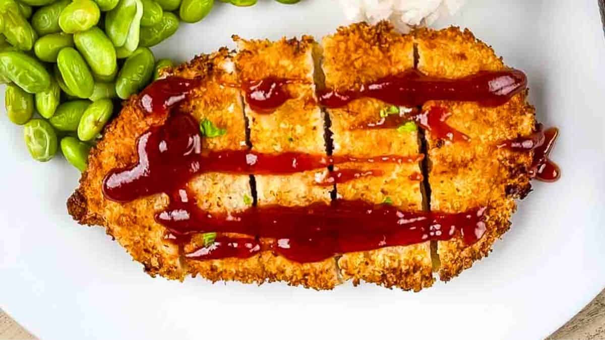 Crispy air fried chicken katsu on a dinner plate, drizzled with homemade tonkatsu sauce.