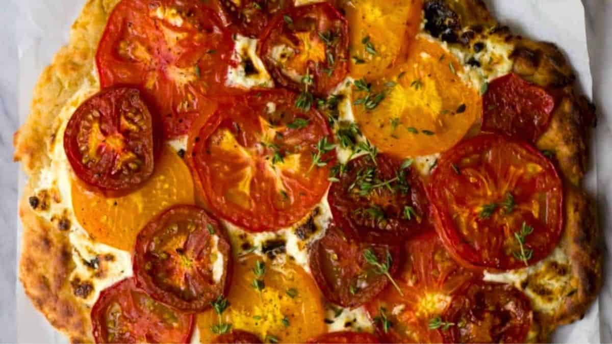 Fresh pizza topped with melted Boursin and colorful tomatoes.