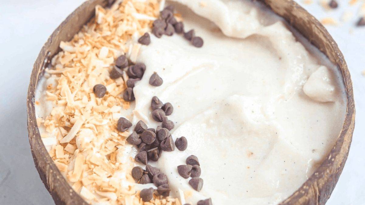 A pristine white smoothie bowl garnished with toasted coconut and chocolate chips.