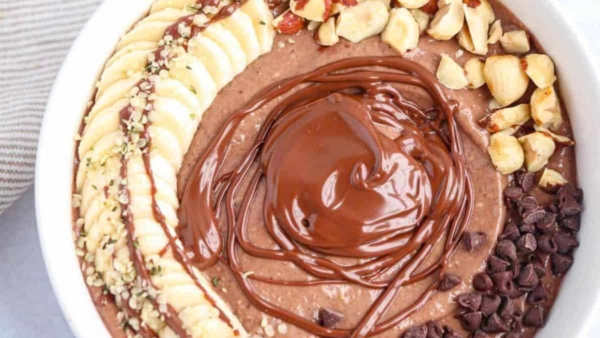 A rich chocolate-hazelnut smoothie bowl topped with banana slices, chopped hazelnuts, and a Nutella drizzle.