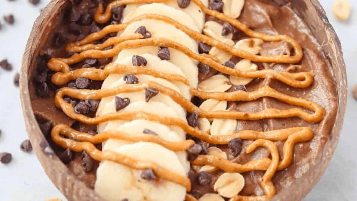 A chocolate-caramel smoothie bowl topped with chopped peanuts, chocolate chips, and caramel drizzle.