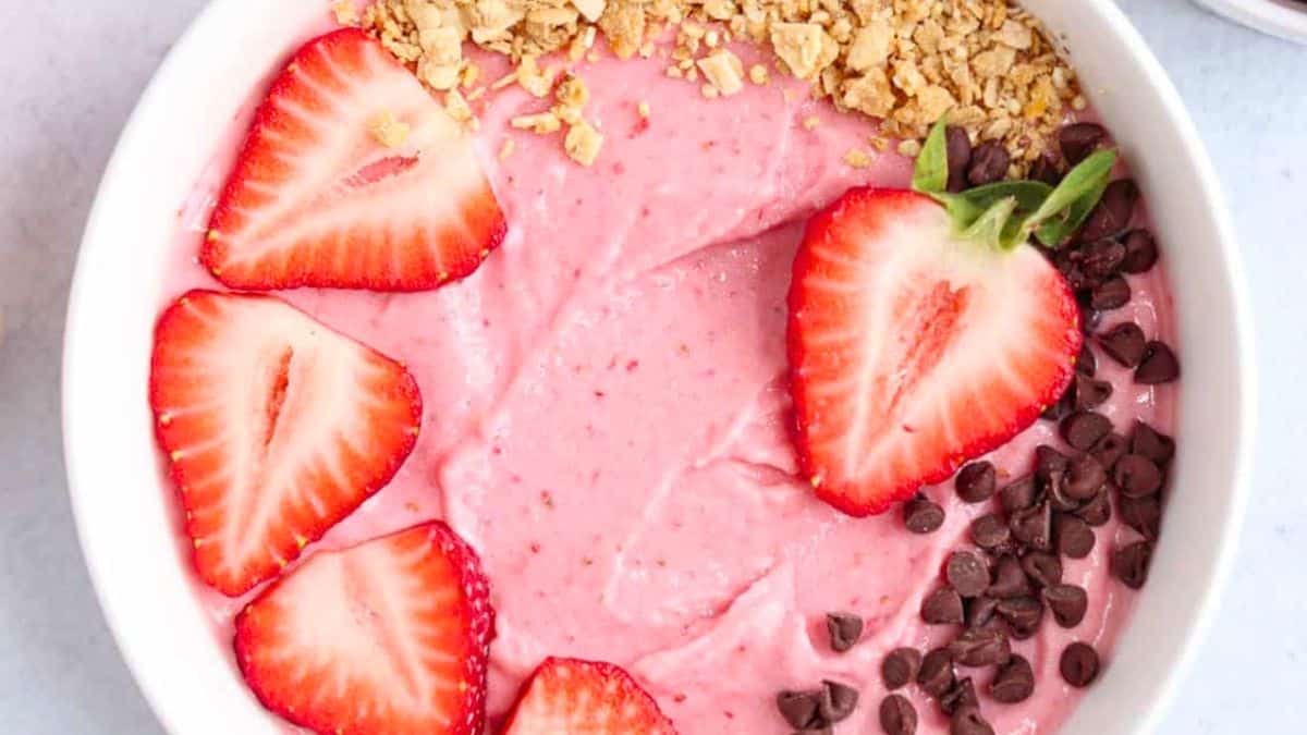 A bright red smoothie bowl topped with fresh strawberries and granola.