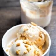 Two scoops of smooth Ninja Creami peanut butter ice cream in white bowl with pint container visible in background, garnished with peanuts.