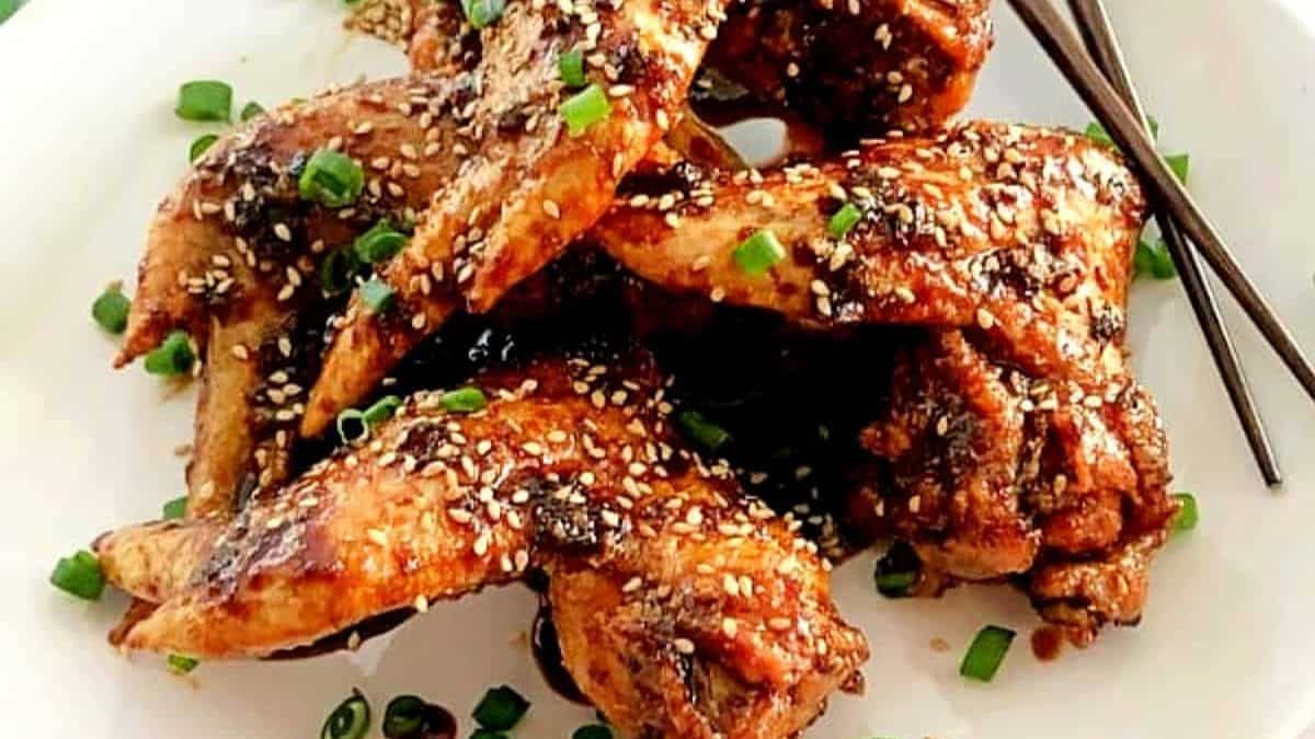 Shiny dark brown wings garnished with white sesame seeds and sliced green onions on a serving plate.