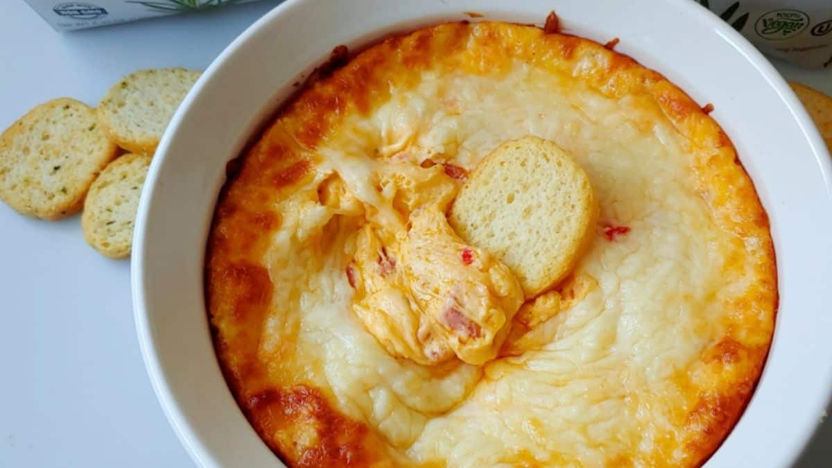 Bubbling hot Italian cheese dip in a baking dish, topped with melted mozzarella and herbs, served with toasted bread slices.
