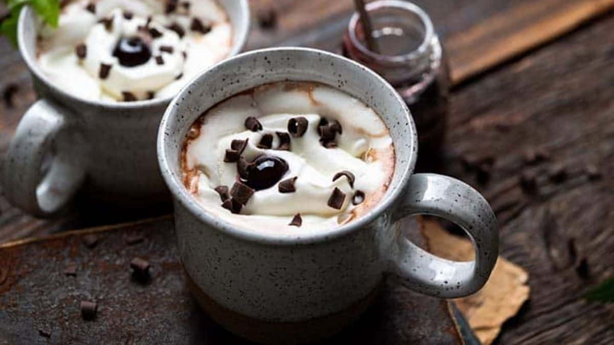 Dark chocolate hot chocolate topped with pillowy whipped cream, a glossy cherry, and chocolate curls.