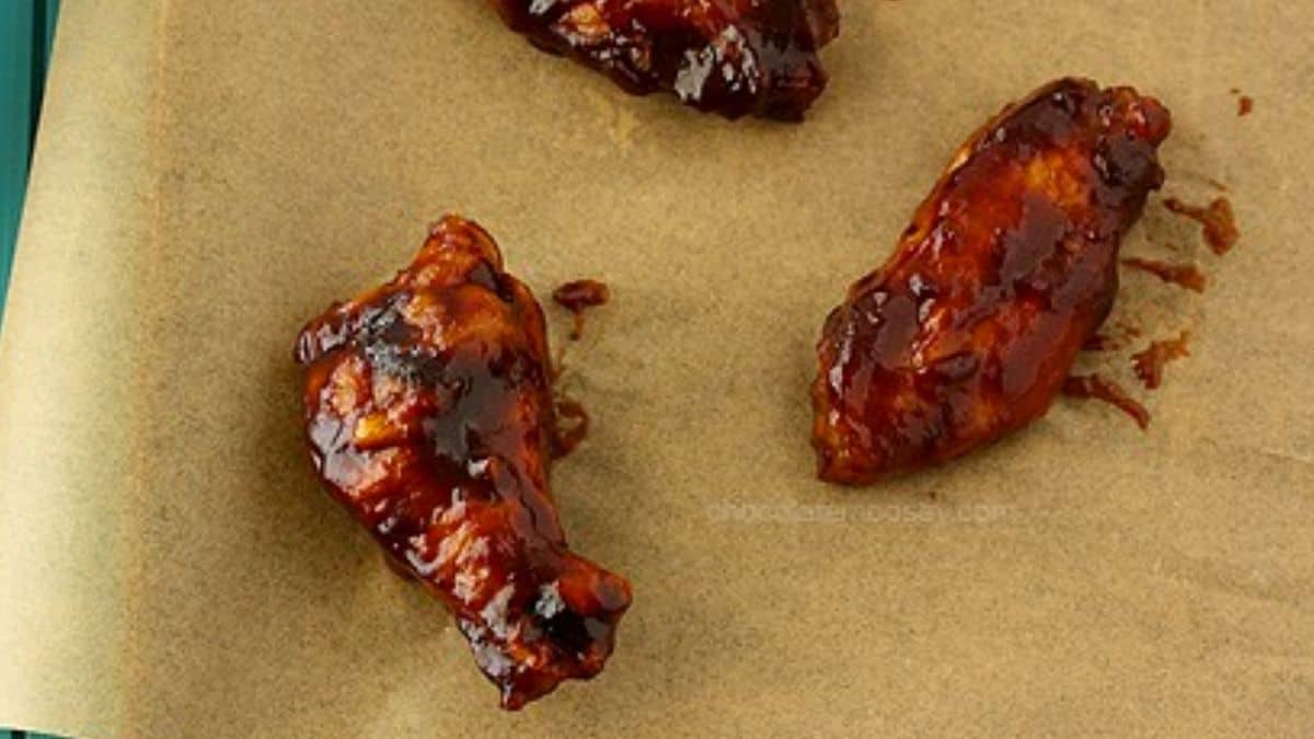 Deep brown, sticky BBQ wings on a serving platter with a brush of honey glaze.