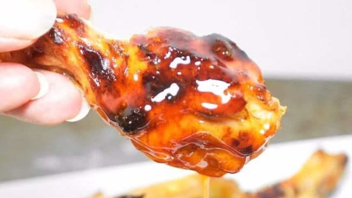 A hand holding a reddish-brown wing with honey drizzling off.