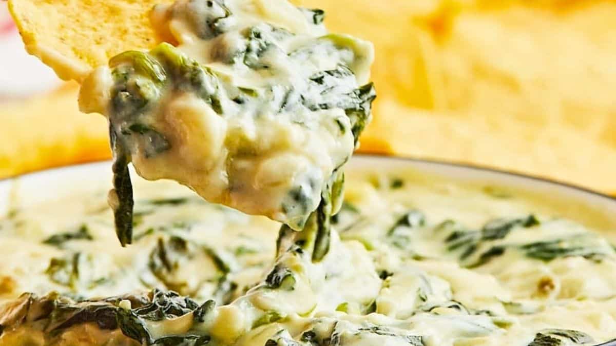 Hot spinach dip being scooped up with a chip.
