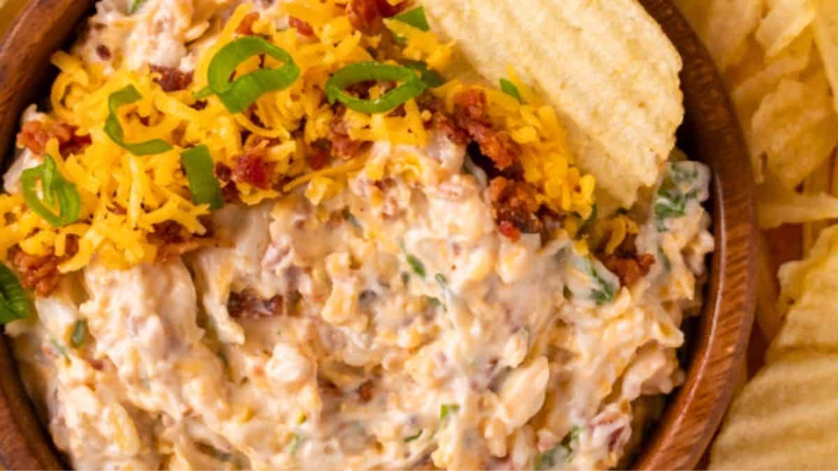 A bowl of million dollar dip garnished with shredded cheese and green onion.