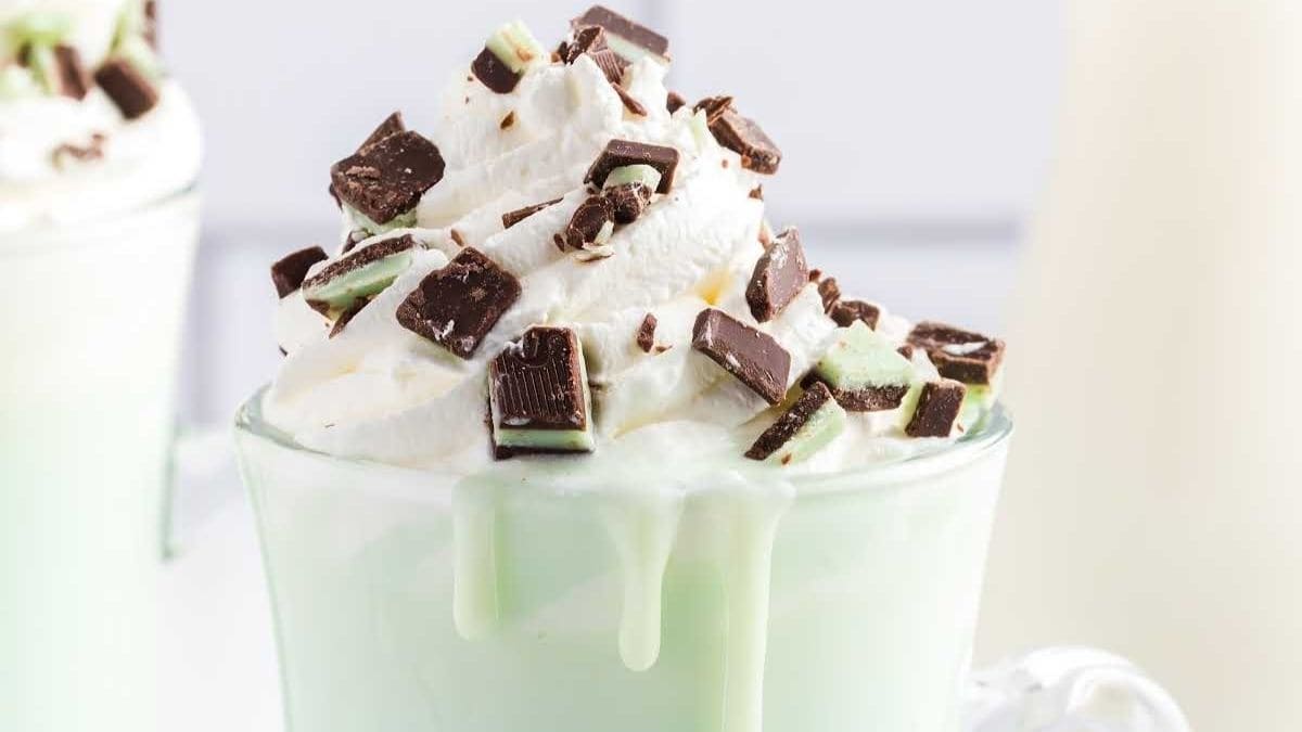 Green mint hot chocolate in a clear glass mug topped with whipped cream and mint chocolate candies.