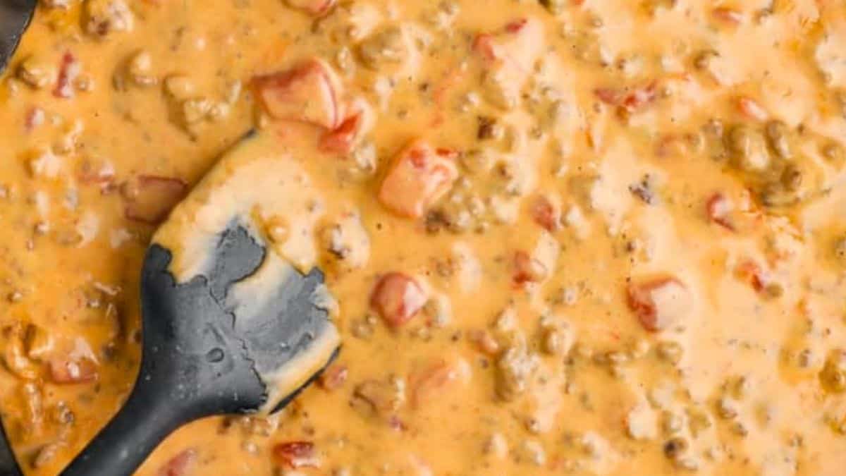 Creamy Rotel dip in a skillet being stirred with a spatula.