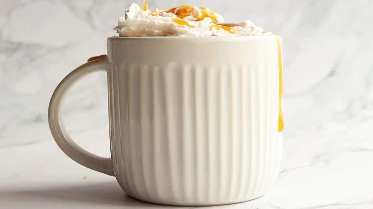 Hot chocolate in a white mug topped with whipped cream and drizzled with caramel sauce.