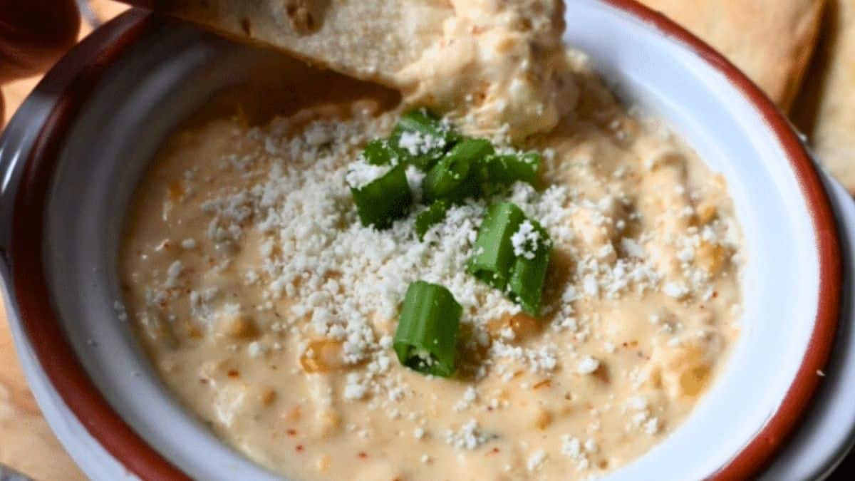 Creamy corn dip in a serving bowl, being scooped up with a chip.