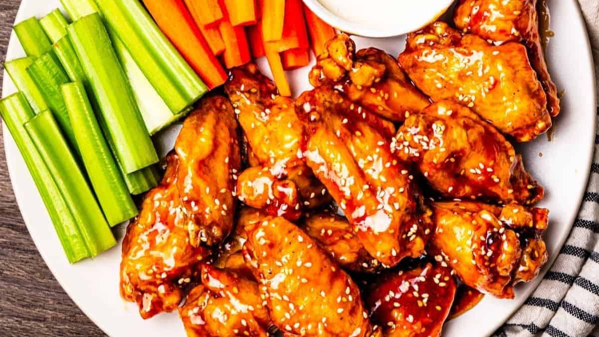 Dark glazed wings with a teriyaki shine on a plate with carrot and celery sticks.