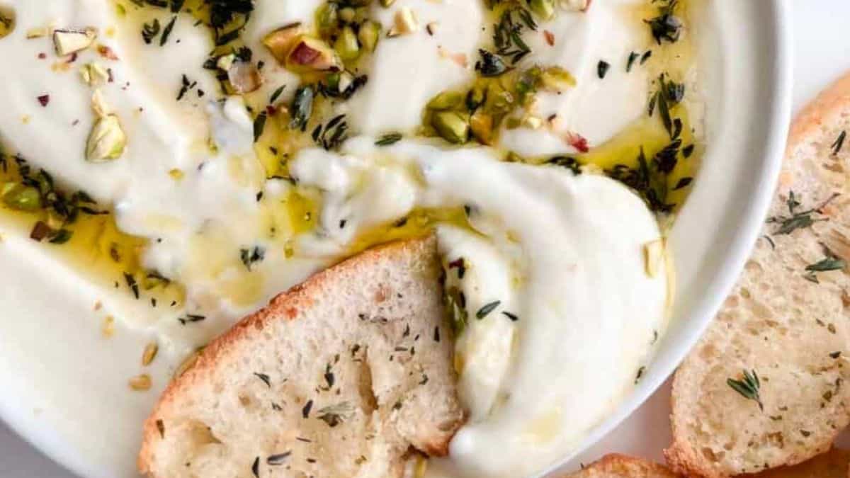 Whipped ricotta dip in a serving bowl with slices of bread for dipping beside it.
