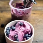 Creamy blueberry ice cream in white bowls with fresh blueberries scattered around.