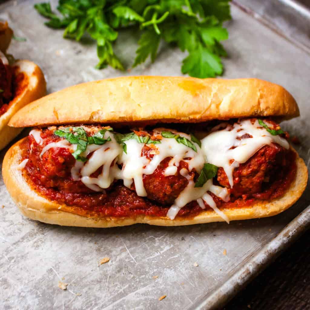 Italian meatball sub on toasted hoagie roll with melted mozzarella and fresh basil, showing sauce dripping from the sides.