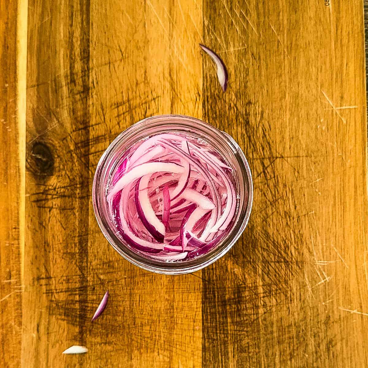 The brine added to a glass jar with red onion slices.