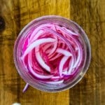 Thinly sliced red onions soaking in vinegar brine in a glass jar.