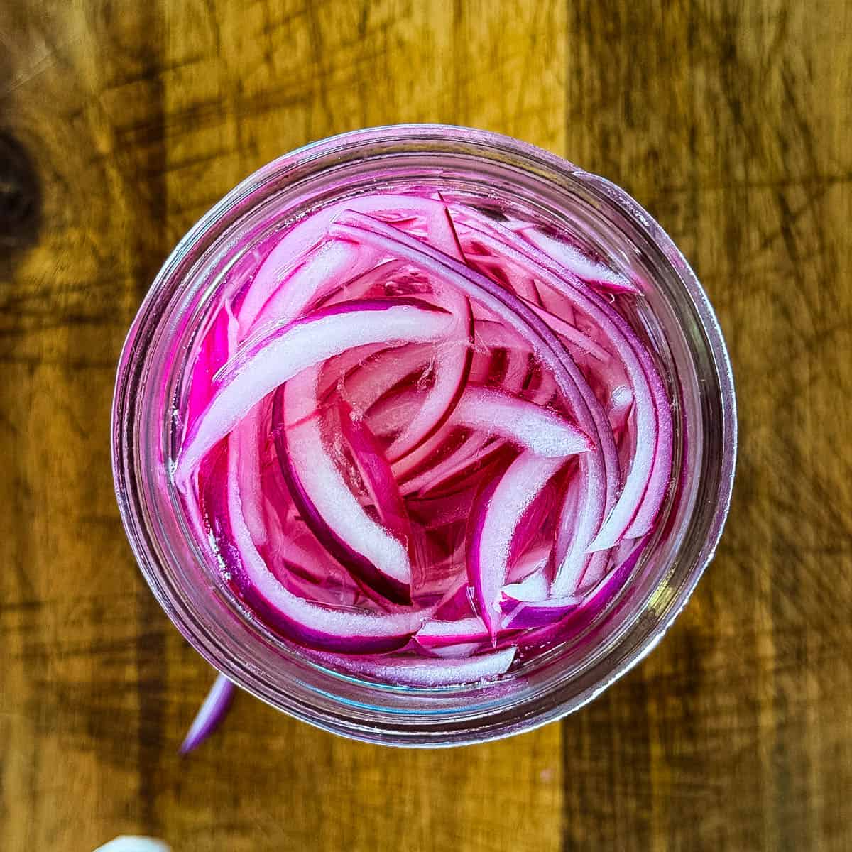 Thinly sliced red onions soaking in vinegar brine in a glass jar.