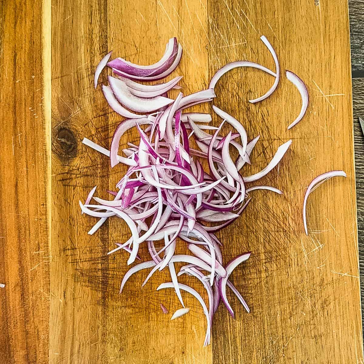 Thinly sliced red onion on a wooden cutting board.