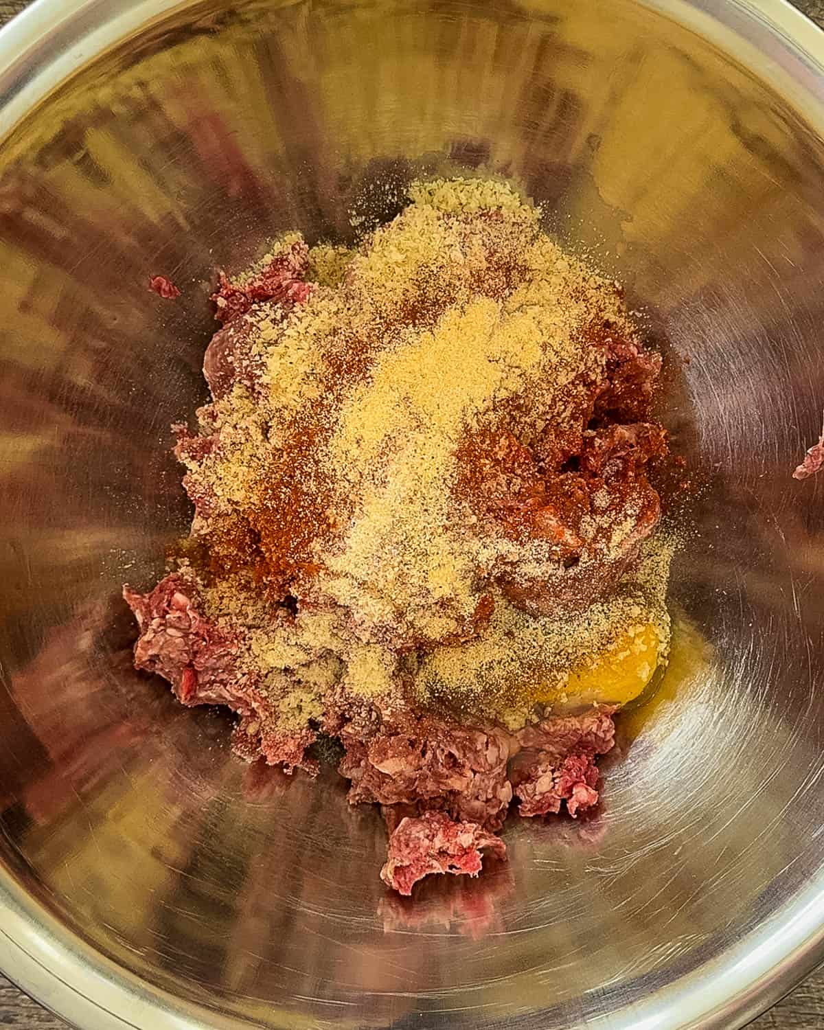 The ingredients for the meatballs in a large stainless steel mixing bowl.