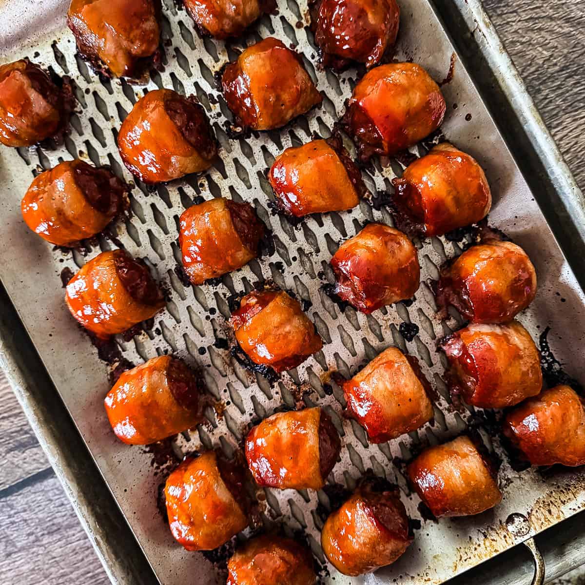 Bacon-wrapped smoked meatballs glazed and served on a grilling tray.
