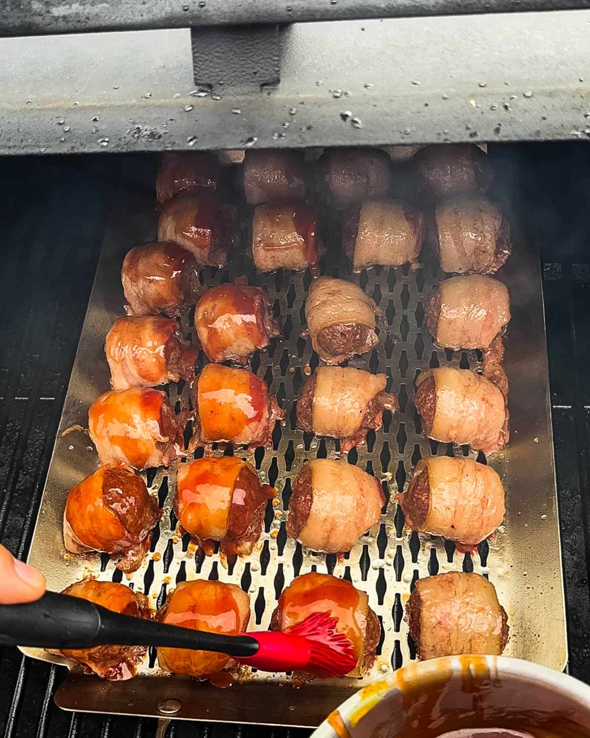 A red brush applying glaze to the meatballs cooking on the smoker.