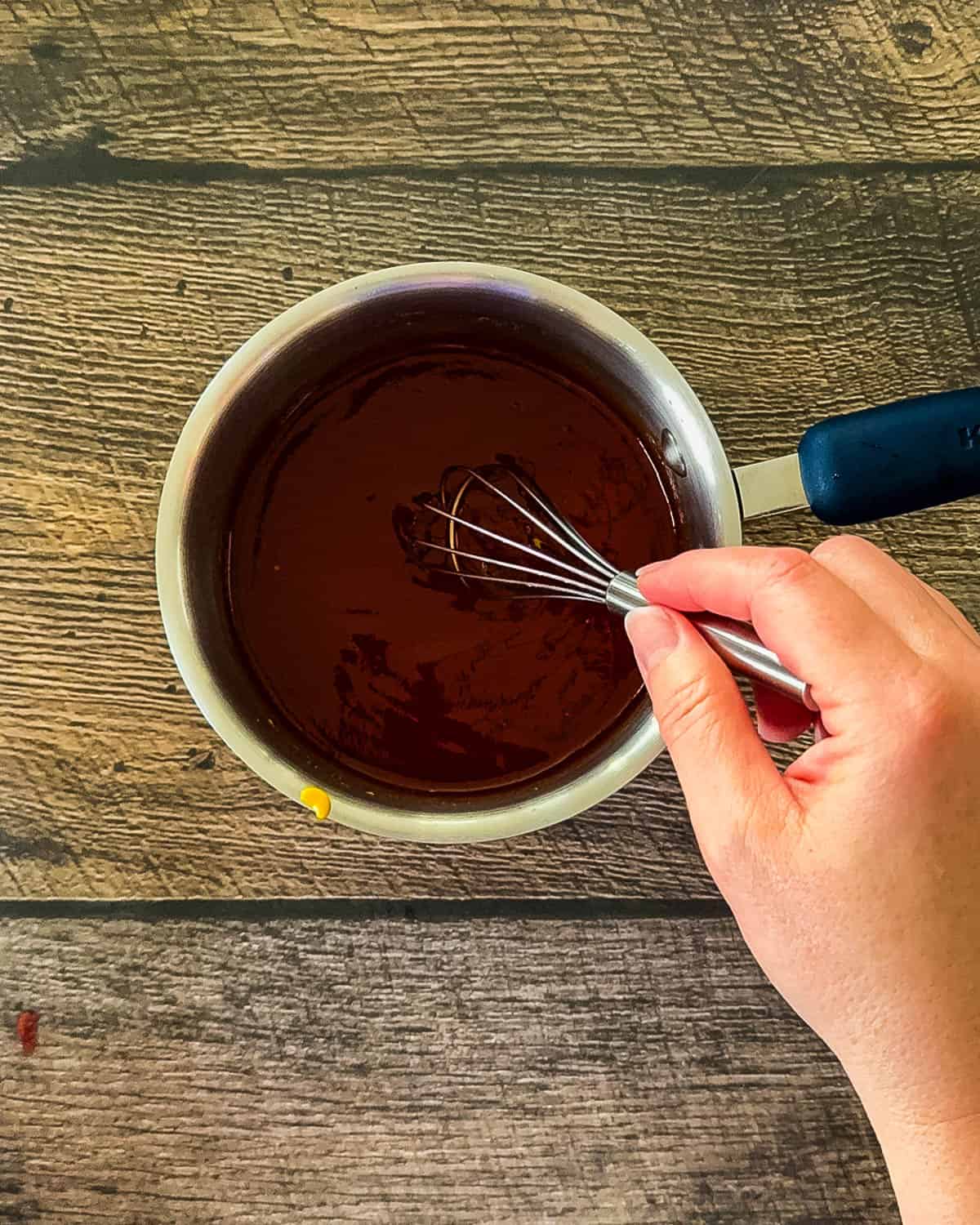 A hand whisking the glaze in a small saucepan.