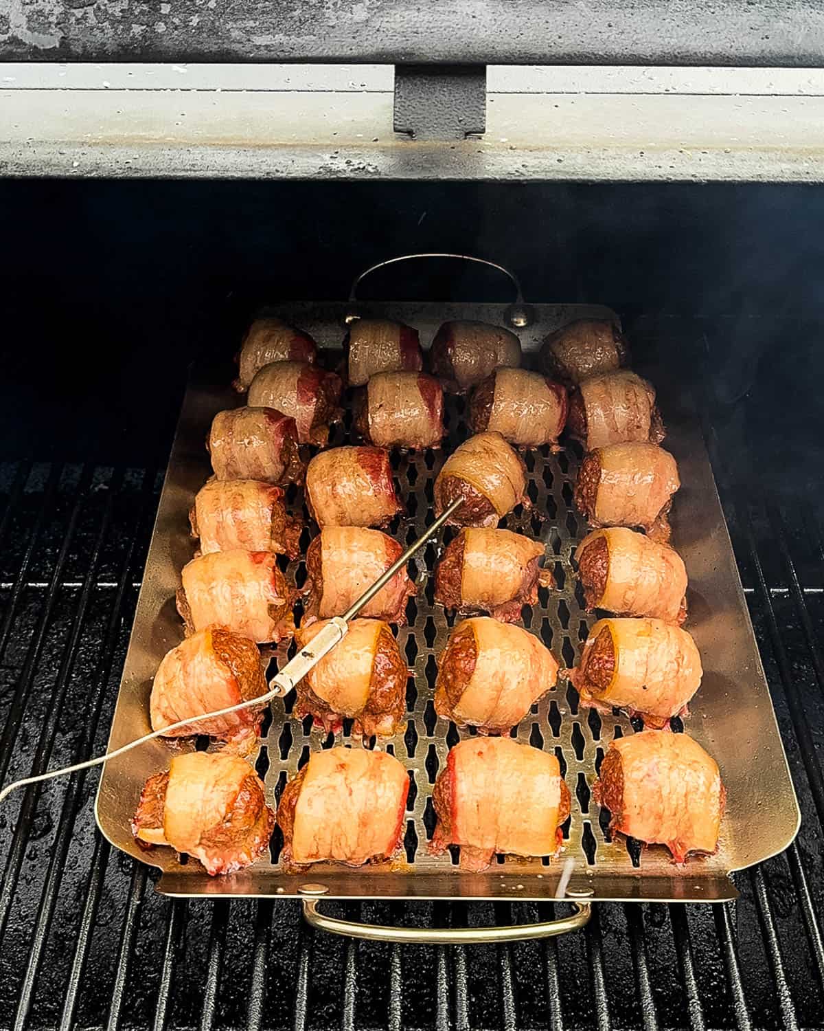 The meatballs smoking on the grill, with a temperature probe inserted in one.
