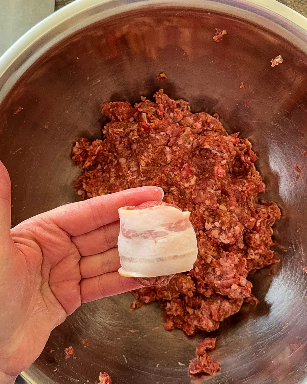 The formed meatball in Jeri's hand wrapped in a half slice of bacon.