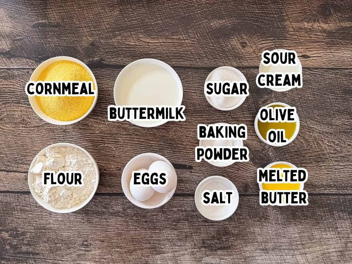 Ingredients for smoked cornbread in bowls with labels – cornmeal, flour, sugar, baking powder, salt, buttermilk, sour cream, eggs, butter, olive oil.