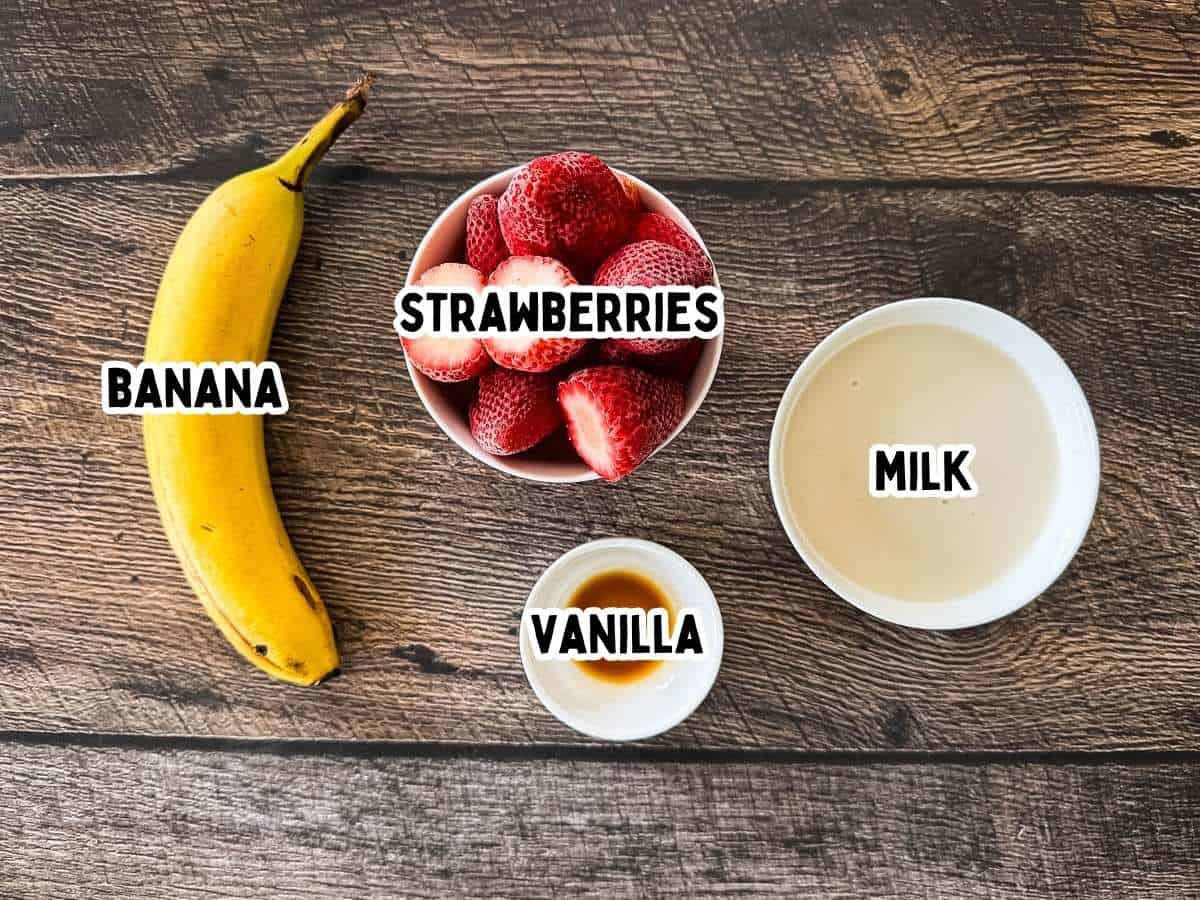 Bowls of ingredients to make a strawberry banana smoothie on a wooden table.