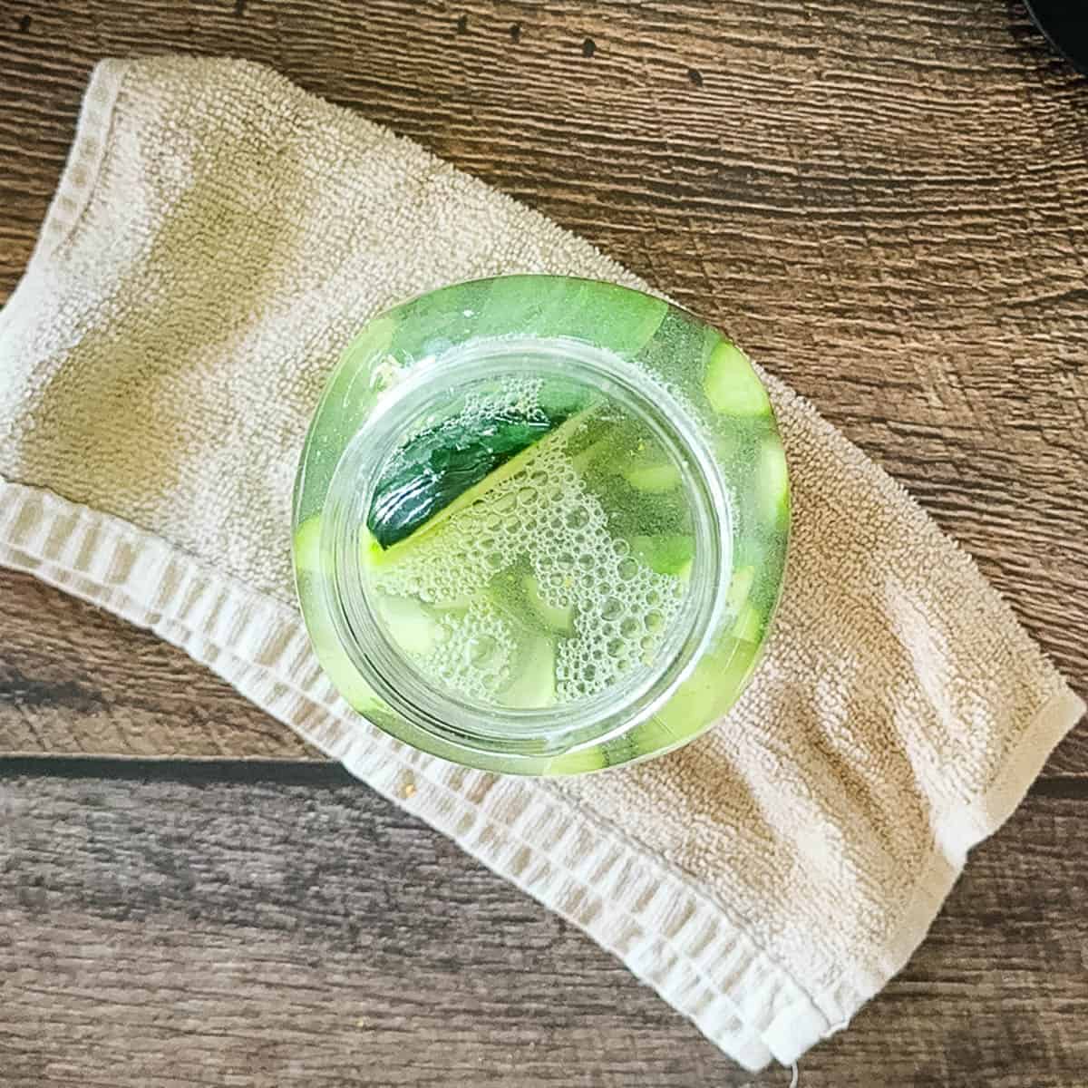 Homemade refrigerator dill pickles in a jar with brine covering fresh cucumbers and garlic.