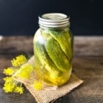 Homemade refrigerator dill pickles in a mason jar with fresh dill flowers on rustic wood background.
