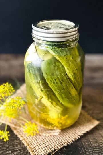Homemade refrigerator dill pickles in a mason jar with fresh dill flowers on rustic wood background.
