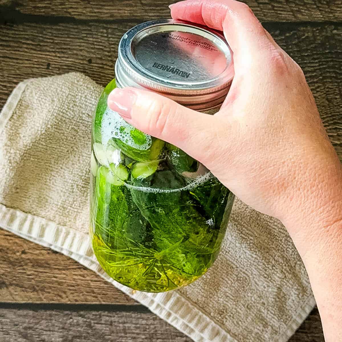 Hand holding a jar of homemade refrigerator dill pickles, shaking to mix the brine.