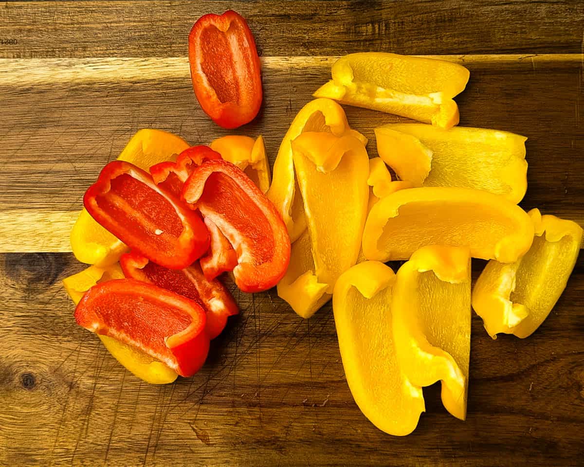 Sliced red and yellow bell peppers on a wooden cutting board, prepped and ready to be seasoned for smoking.