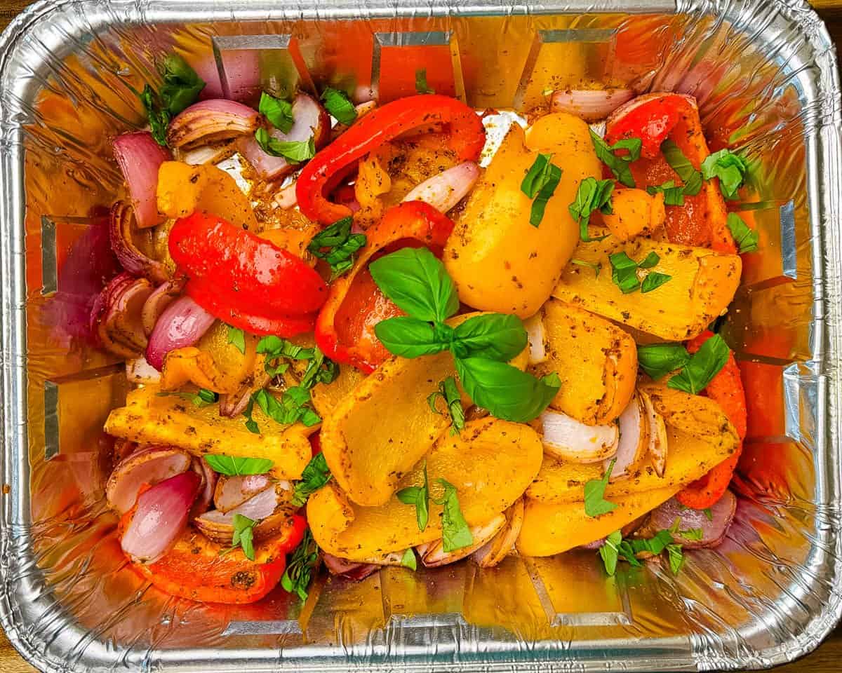 Smoked peppers and onions in a foil pain, garnished with fresh basil.