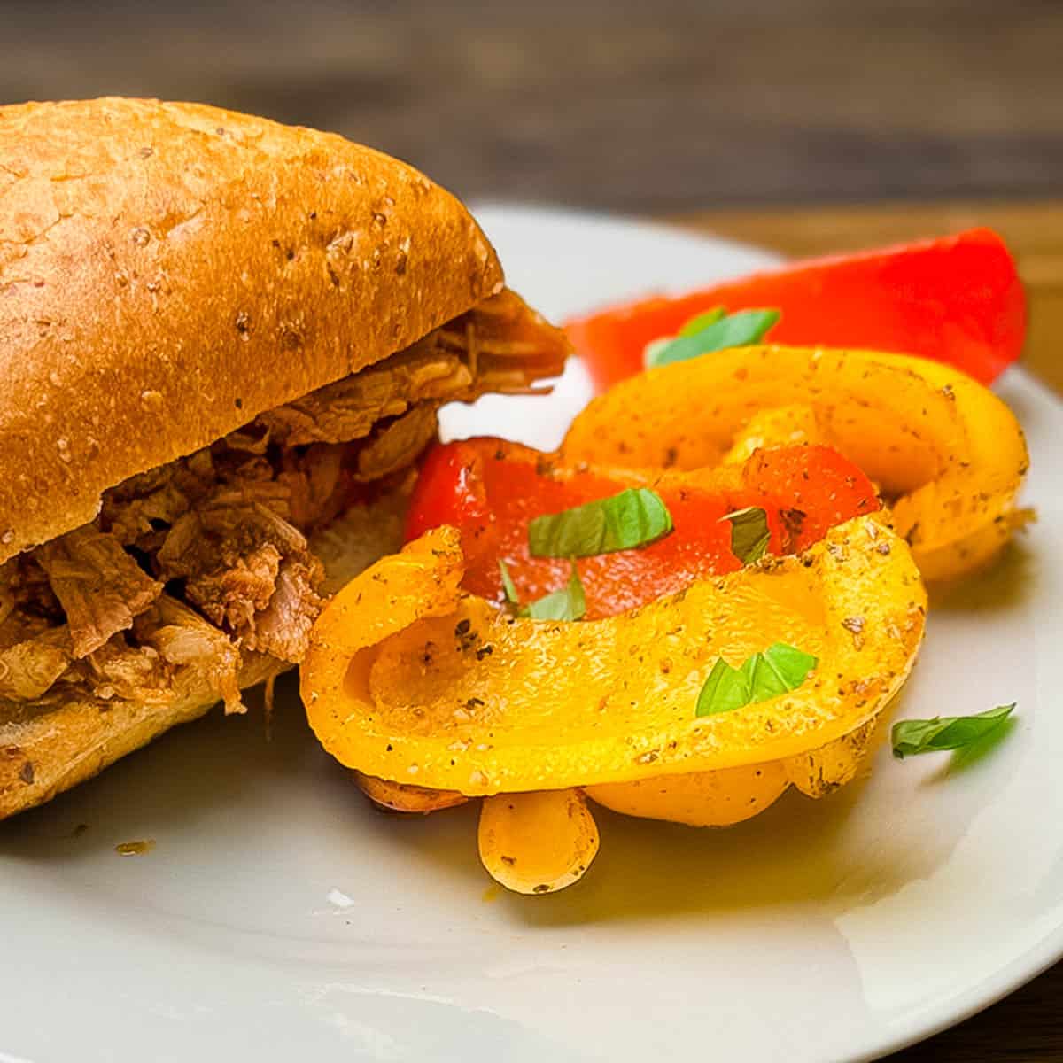 Smoked bell peppers and onions served on a plate next to a sandwich on a seeded whole wheat bun.
