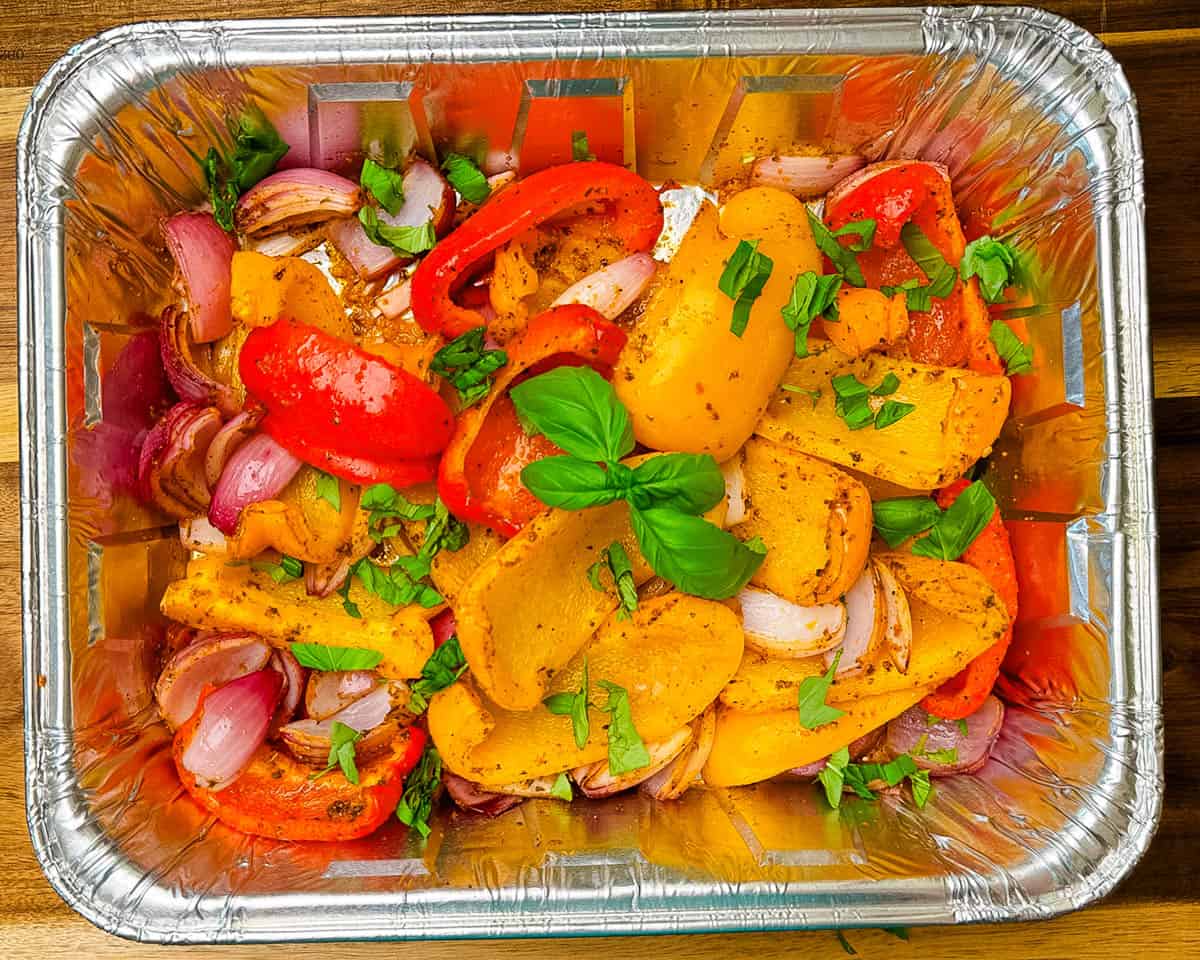 Smoked red onions and bell peppers with light char marks inside a foil pan, just pulled off the smoker.
